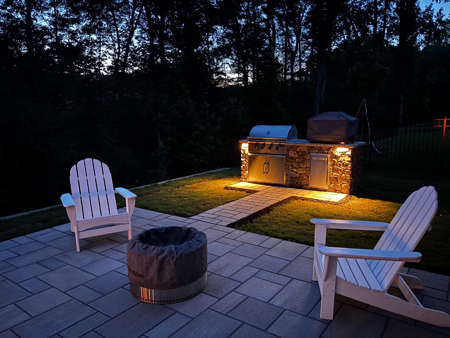 Illuminated outdoor kitchen on a paver patio at dusk